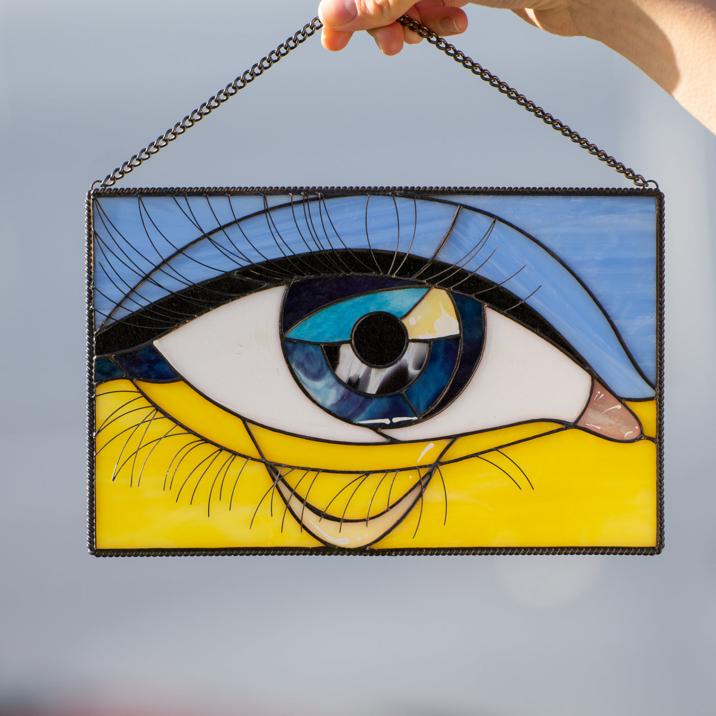 Stained glass window panel depicting Ukrainian flag and a crying eye in the middle