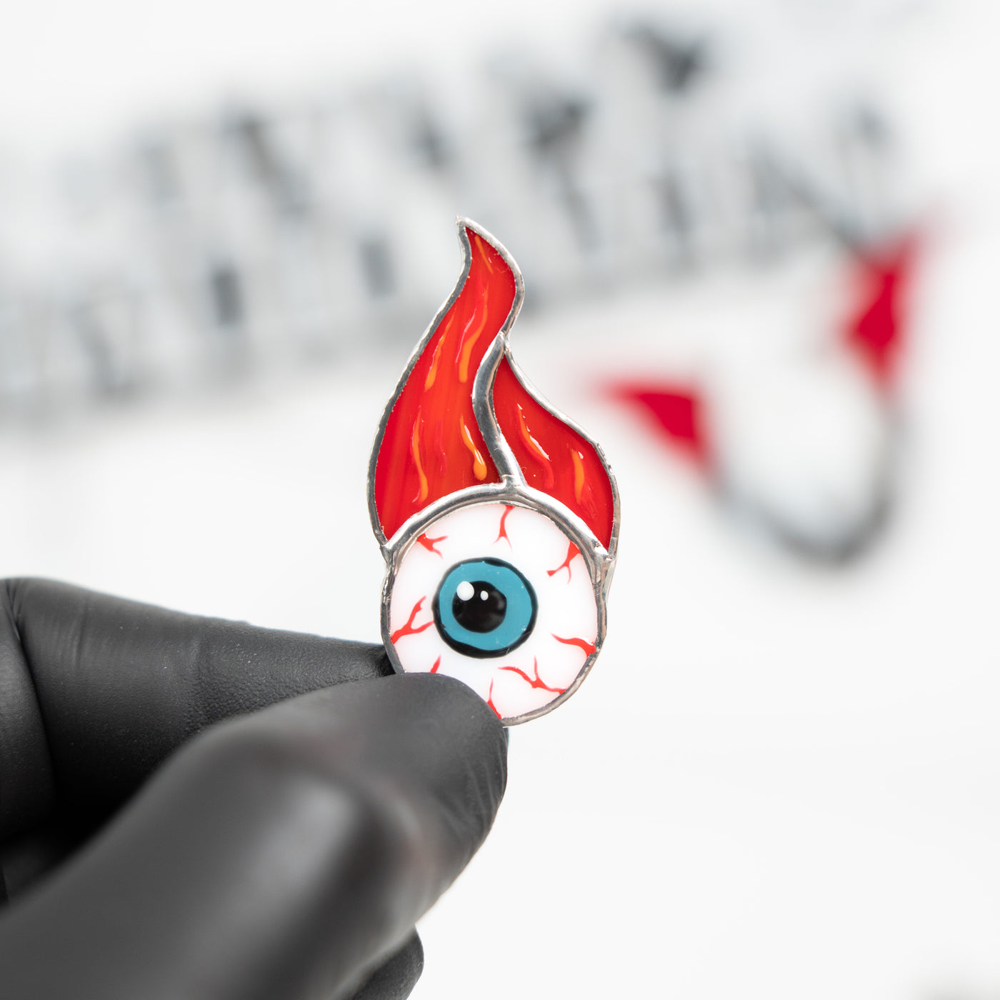 Stained glass Halloween pin of a torn out eye with fire above