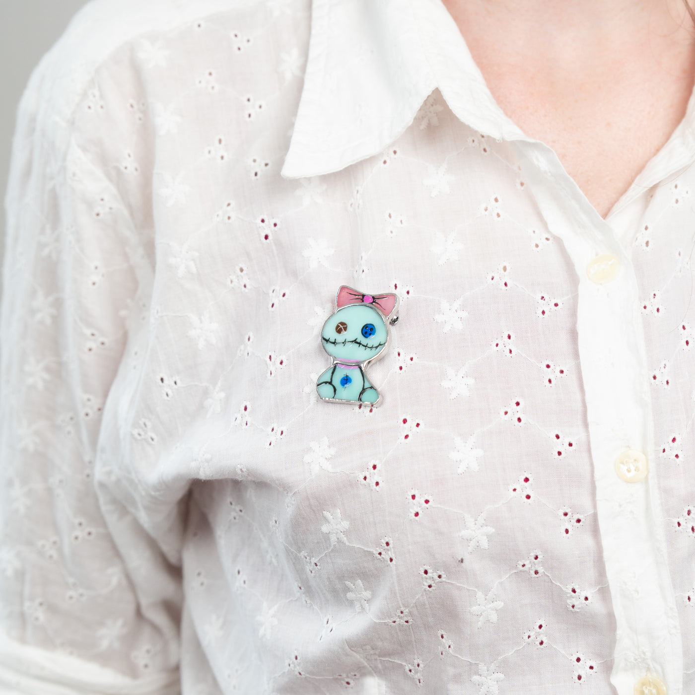 Stained glass turquoise toy with pink bow brooch on a white shirt