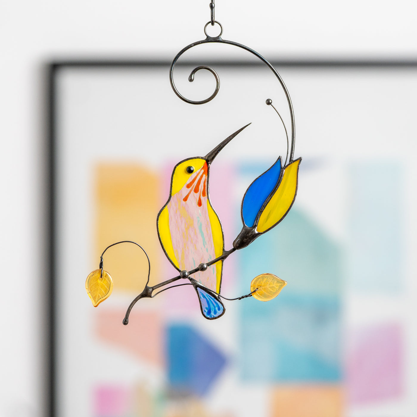 Sitting on the branch hummingbird with blue and yellow flower suncatcher of stained glass