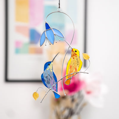 Stained glass window hanging of blue and yellow hummingbirds with the blue flower