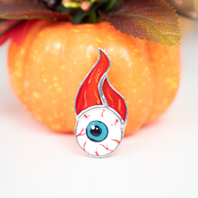 Halloween torn out eye with fire above brooch of stained glass