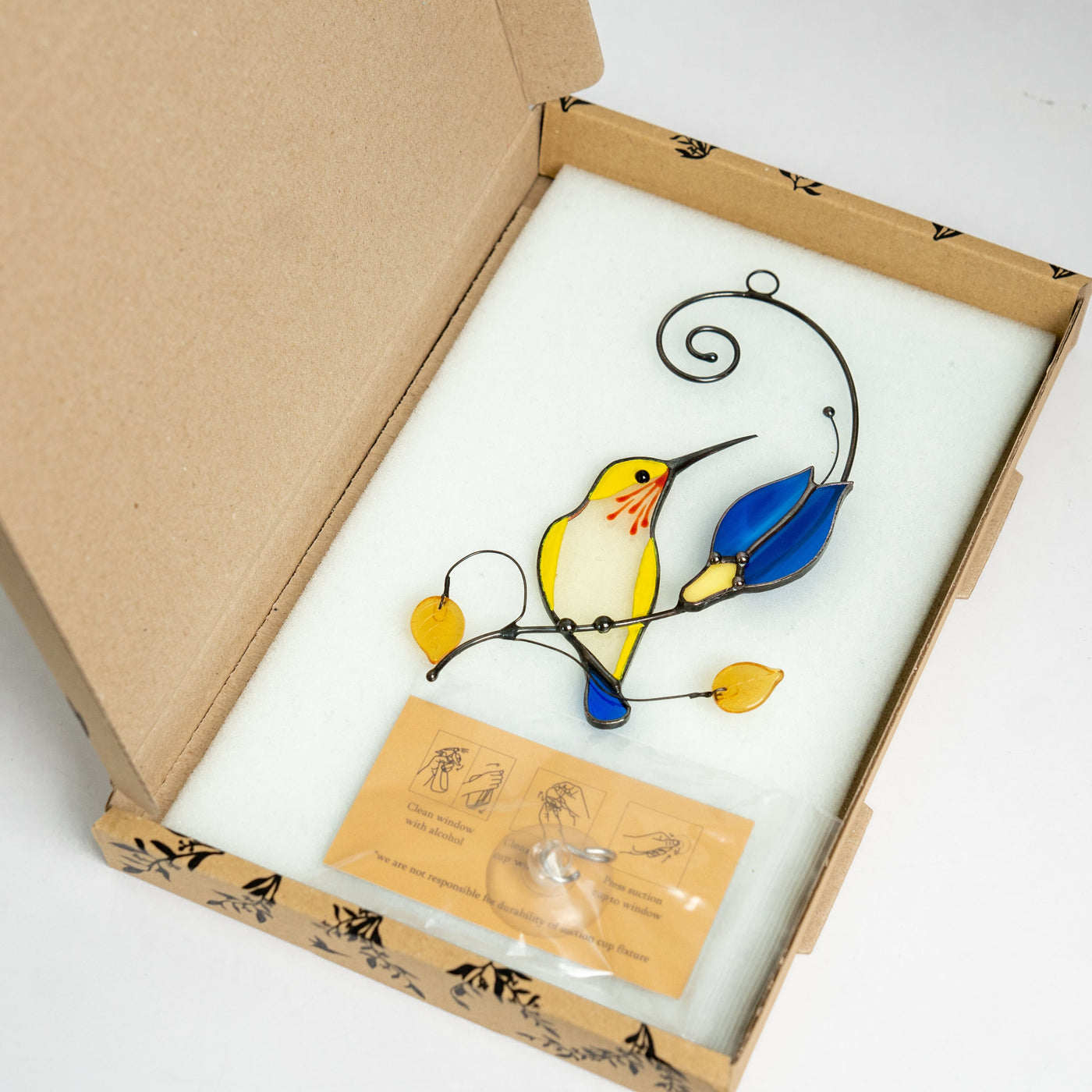 Stained glass yellow hummingbird with the blue flower in the brand box