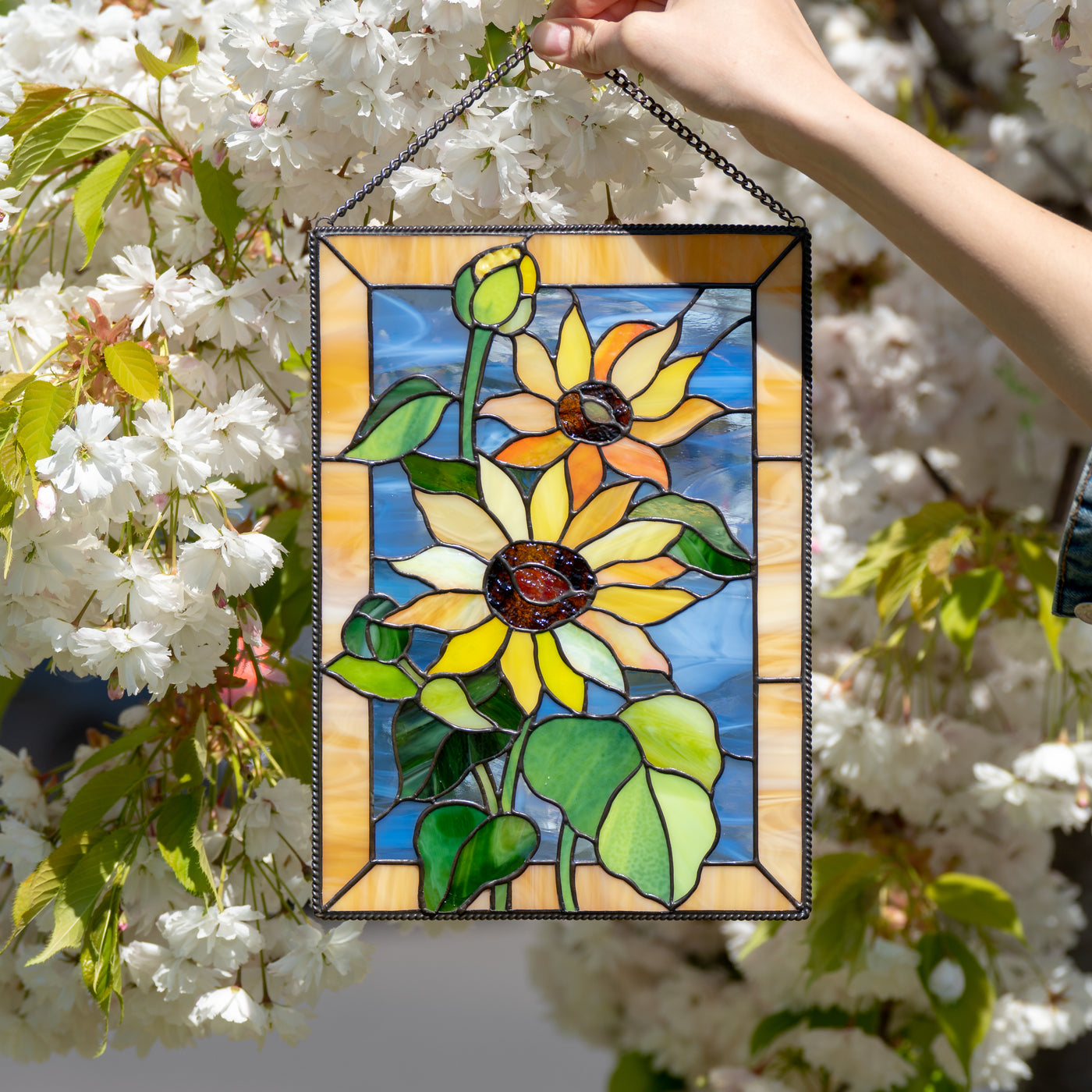 Stained glass window hanging with blue and yellow background depicting sunflowers