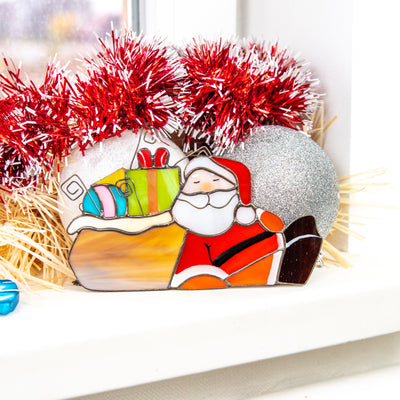 Stained glass Santa lying next to the gifts window hanging for Christmas home decor