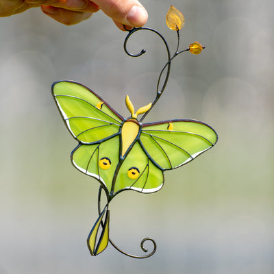 Stained glass window hanging of a luna moth butterfly on the branch with yellow leaves