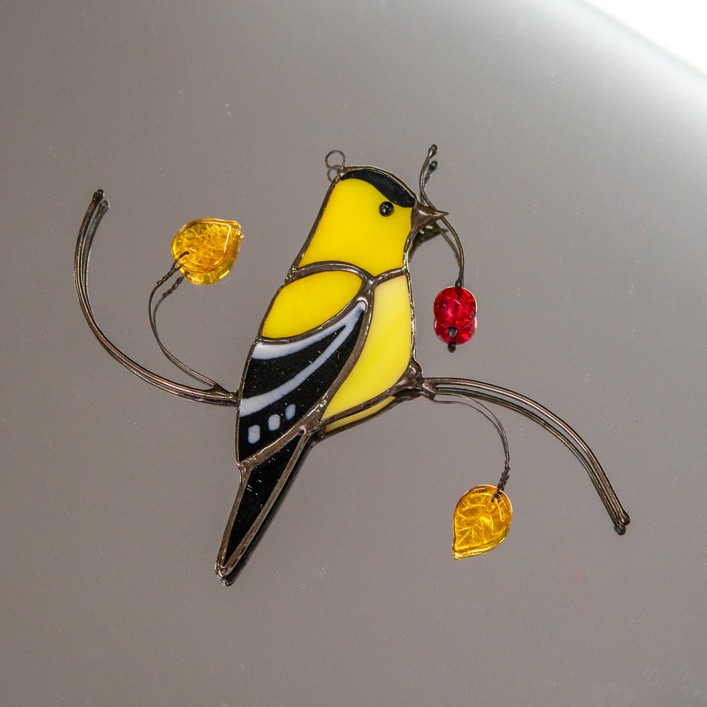 Stained glass goldfinch sitting on the branch with leaves and berries window hanging