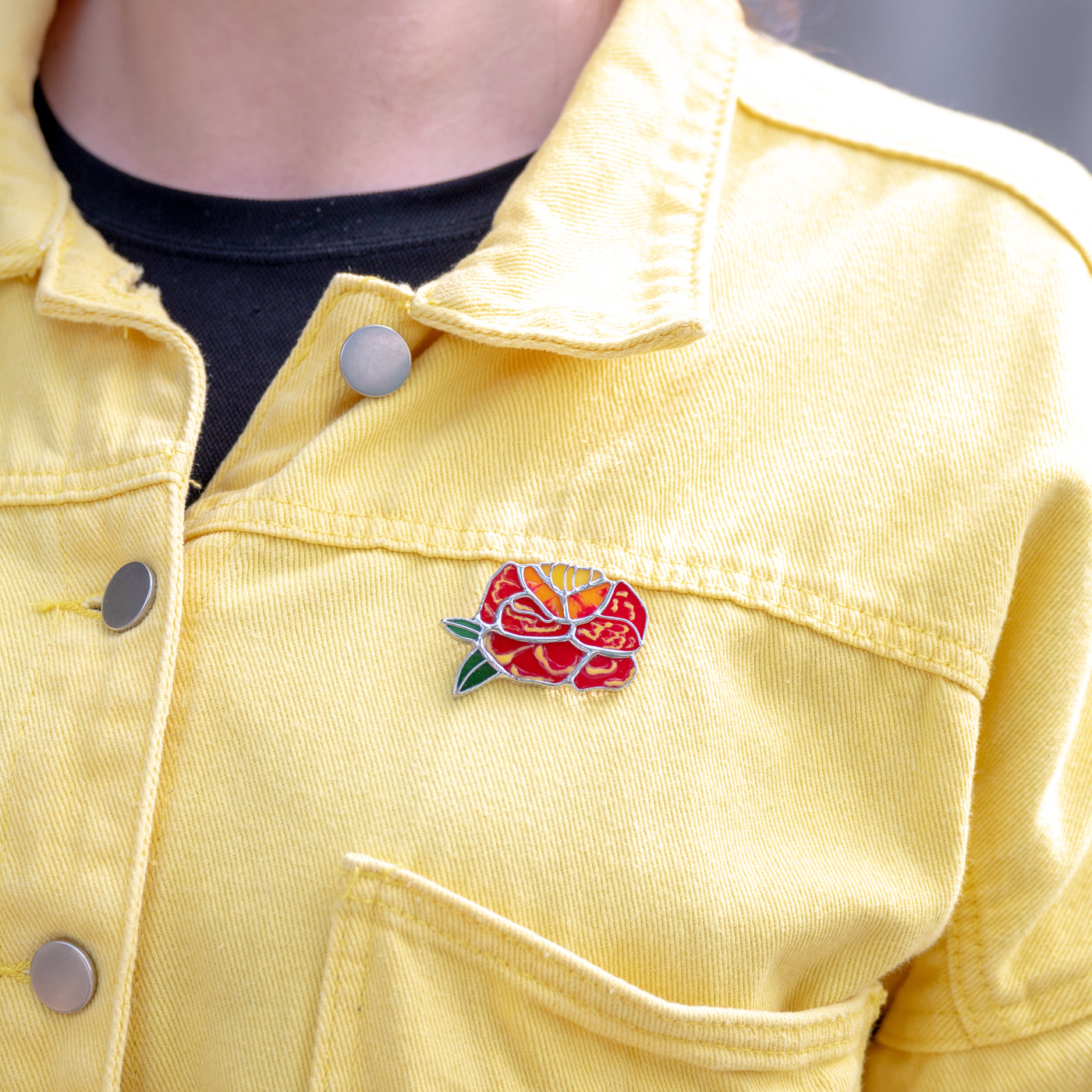 Stained glass marigold flower pin on a yellow jacket