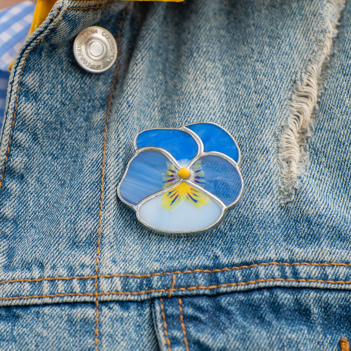Stained glass blue pansy flower brooch on a jeans jacket