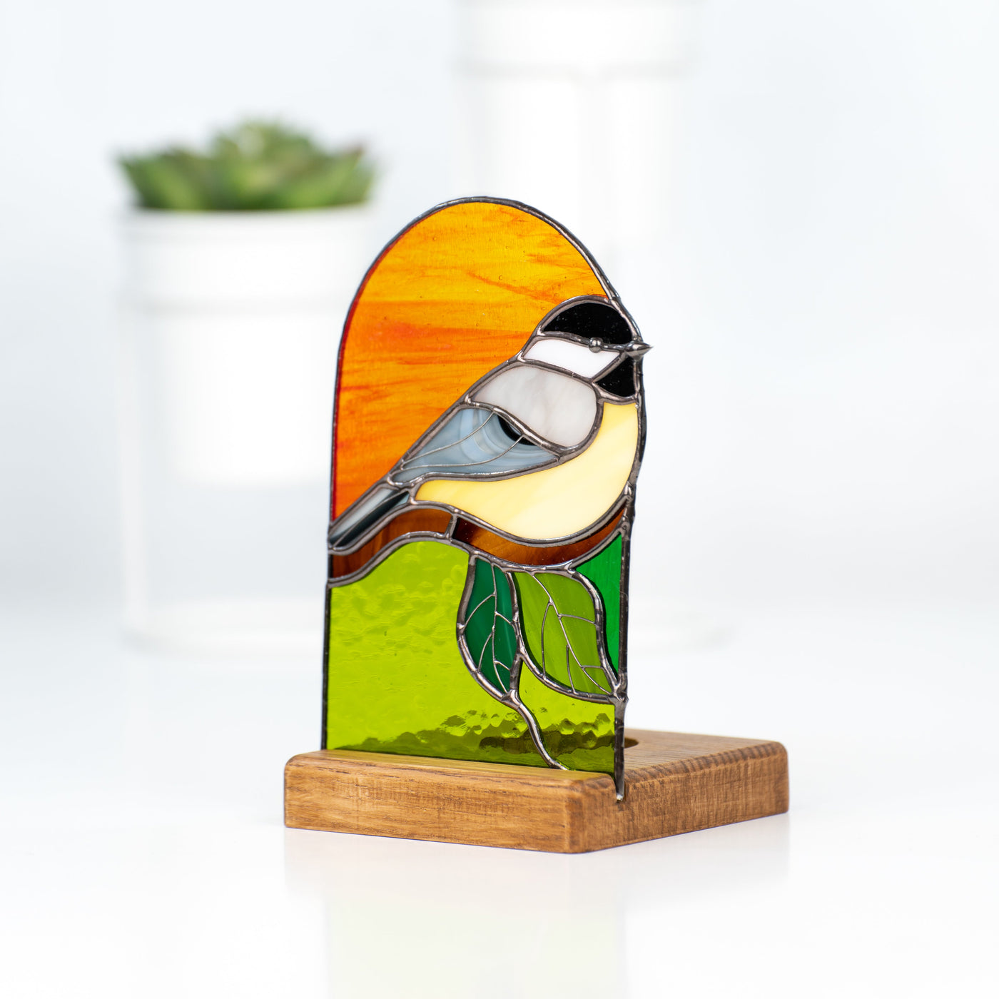 Stained glass panel depicting a chickadee on orange and green background side-view