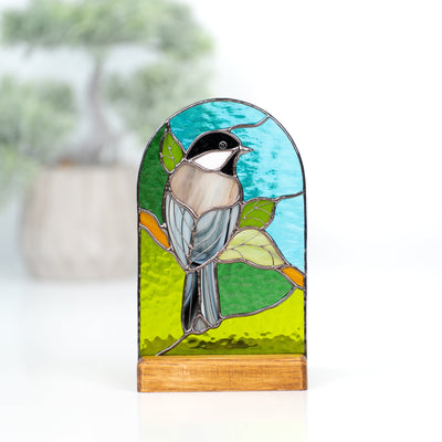 Stained glass panel in a wooden base depicting a chickadee on the nature background