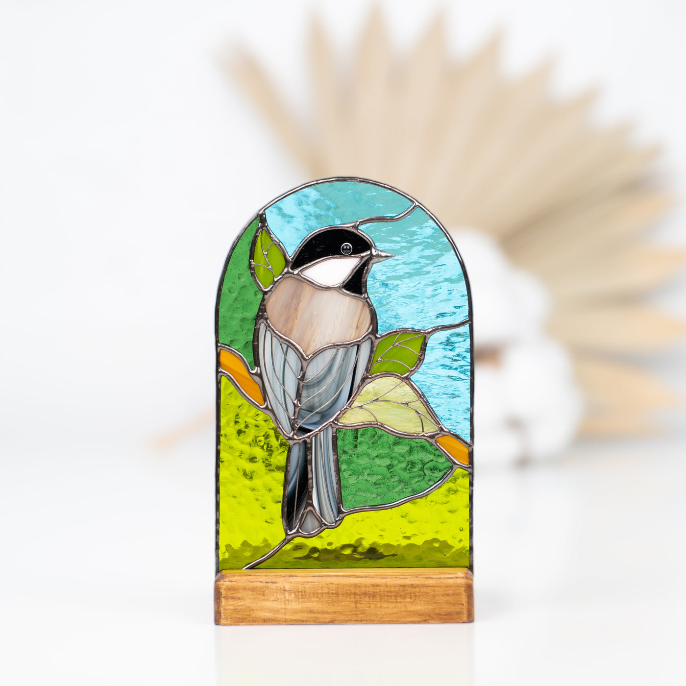 Panel in a wooden base depicting a chickadee on the nature background of stained glass