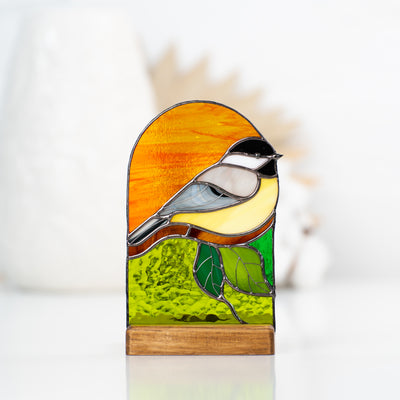 Stained glass panel depicting a chickadee on orange and green background with a wooden base for candle