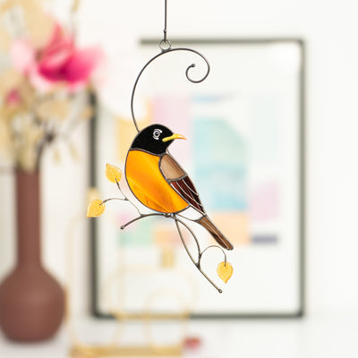 Looking right Baltimore oriole sitting on the branch with yellow leaves window hanging of stained glass