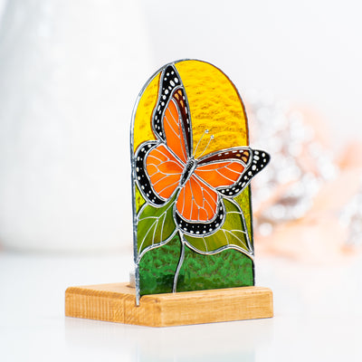 Side-view of a stained glass panel in a wooden base with the candle behind depicting monarch butterfly