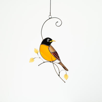 Stained glass window hanging of a looking right Baltimore oriole sitting on the branch with yellow leaves 