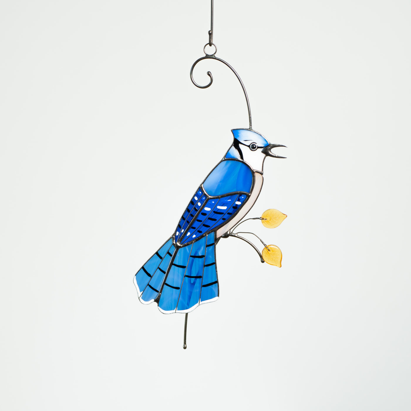 Blue jay with feathery tail sitting on the branch window hanging of stained glass