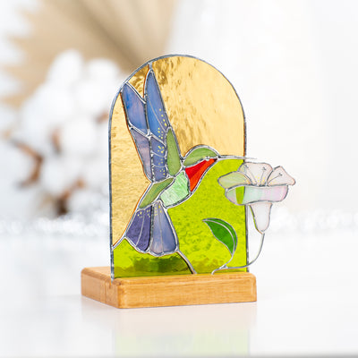 Stained glass candle-lit panel in a wooden base depicting a flying hummingbird and the flower
