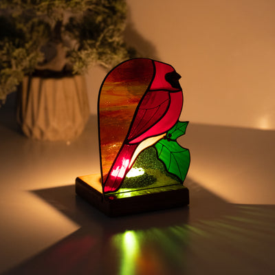 Candle-lit stained glass panel depicting red cardinal in the dark