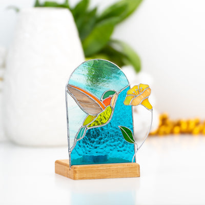 Stained glass candle-lit panel in a wooden base depicting a flying hummingbird and yellow flower