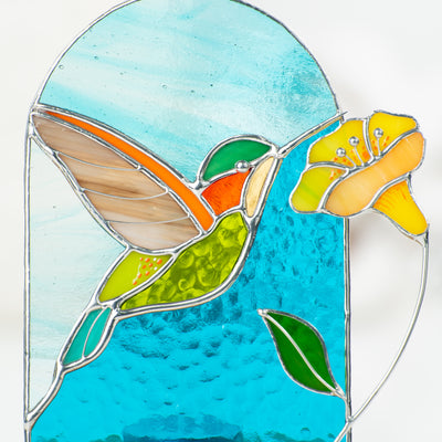 Zoomed stained glass hummingbird with yellow flower depicted on a panel