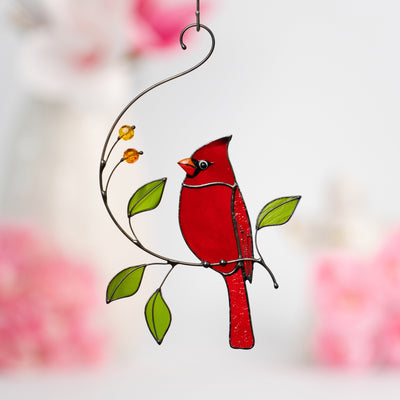 Stained glass window hanging of a red cardinal sitting on the branch and looking left