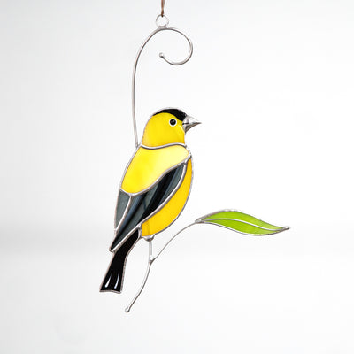 Stained glass goldfinch sitting on the branch with a green leaf suncatcher