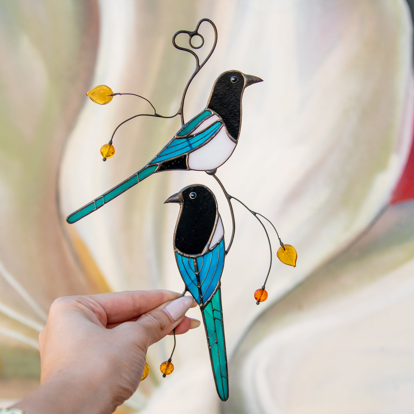 Stained glass suncatcher of two magpies sitting on the branch with leaves and berries