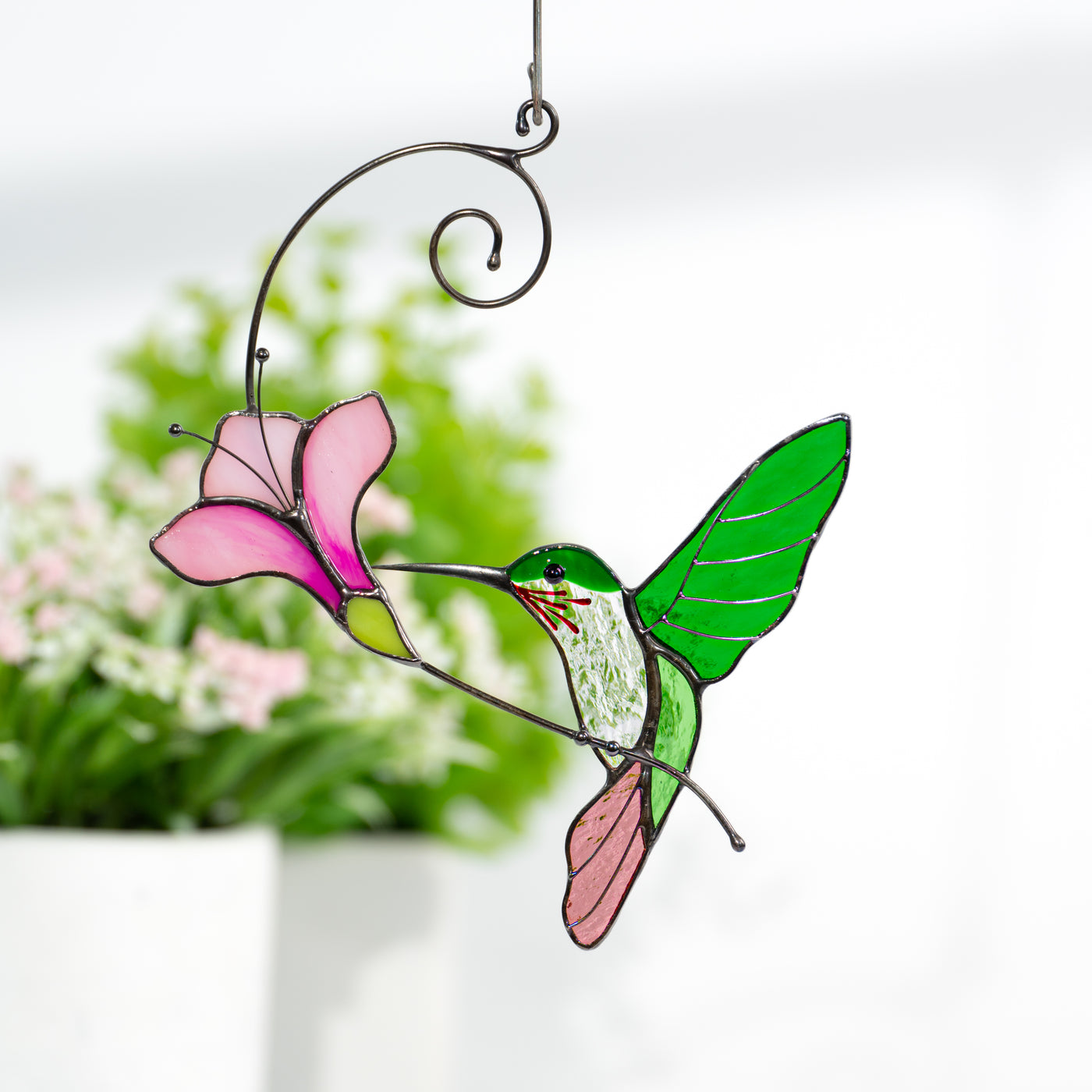 Stained glass window hanging of a green hummingbird with purplish flower