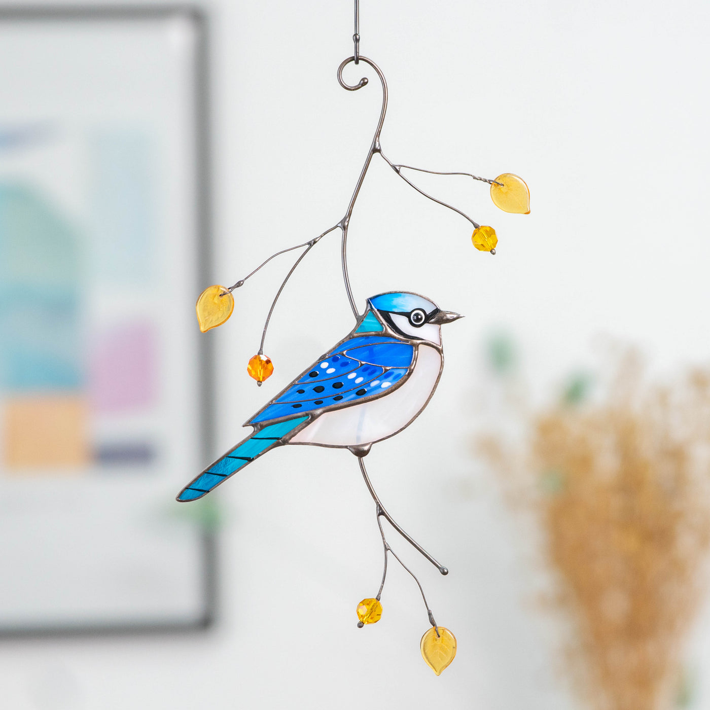 Window hanging of a stained glass blue jay sitting on the branch with leaves and berries