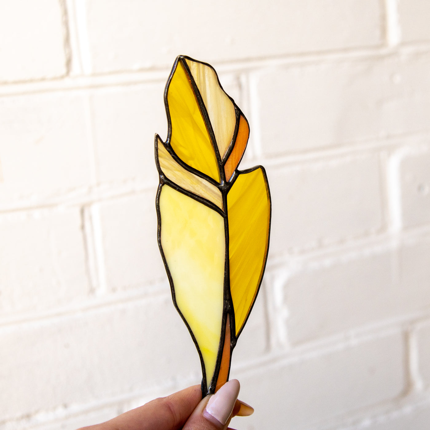 Stained glass feather suncatcher of yellow color with whity and orange parts