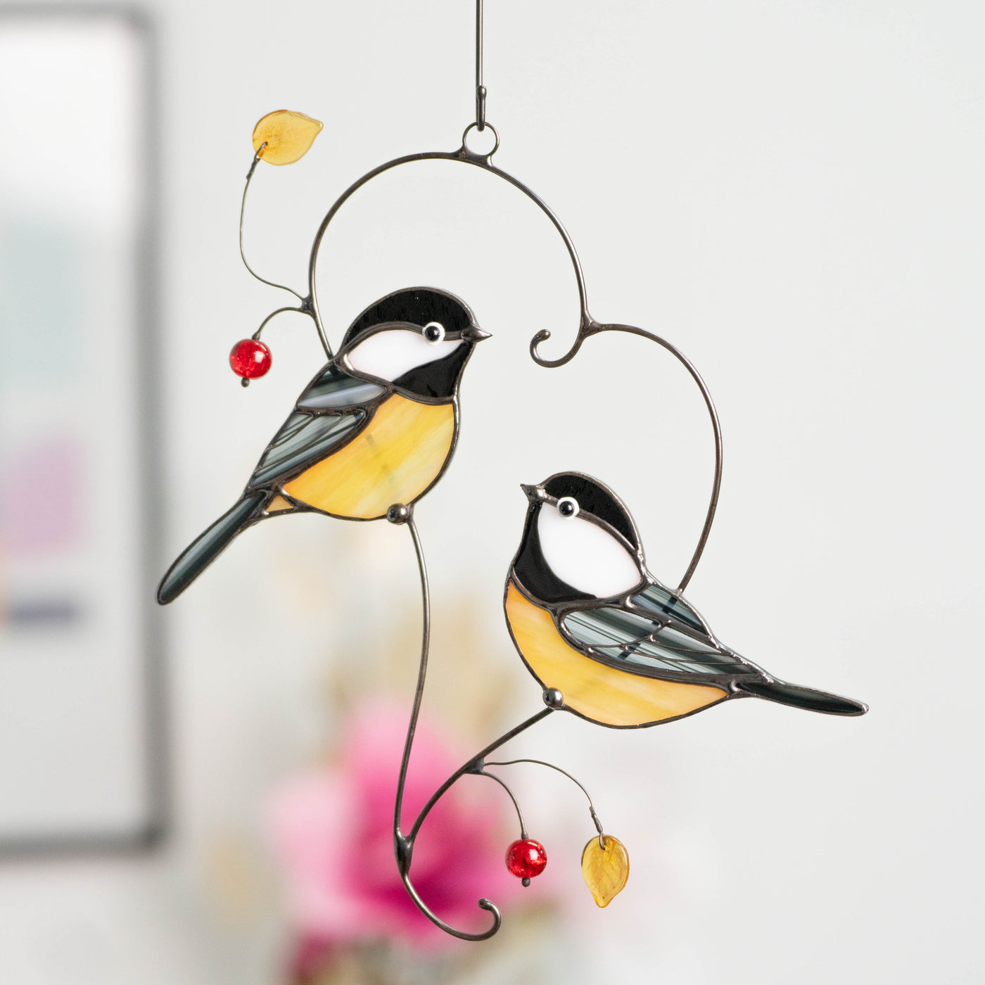 Chickadees sitting on the heart-shaped branch suncatcher of stained glass