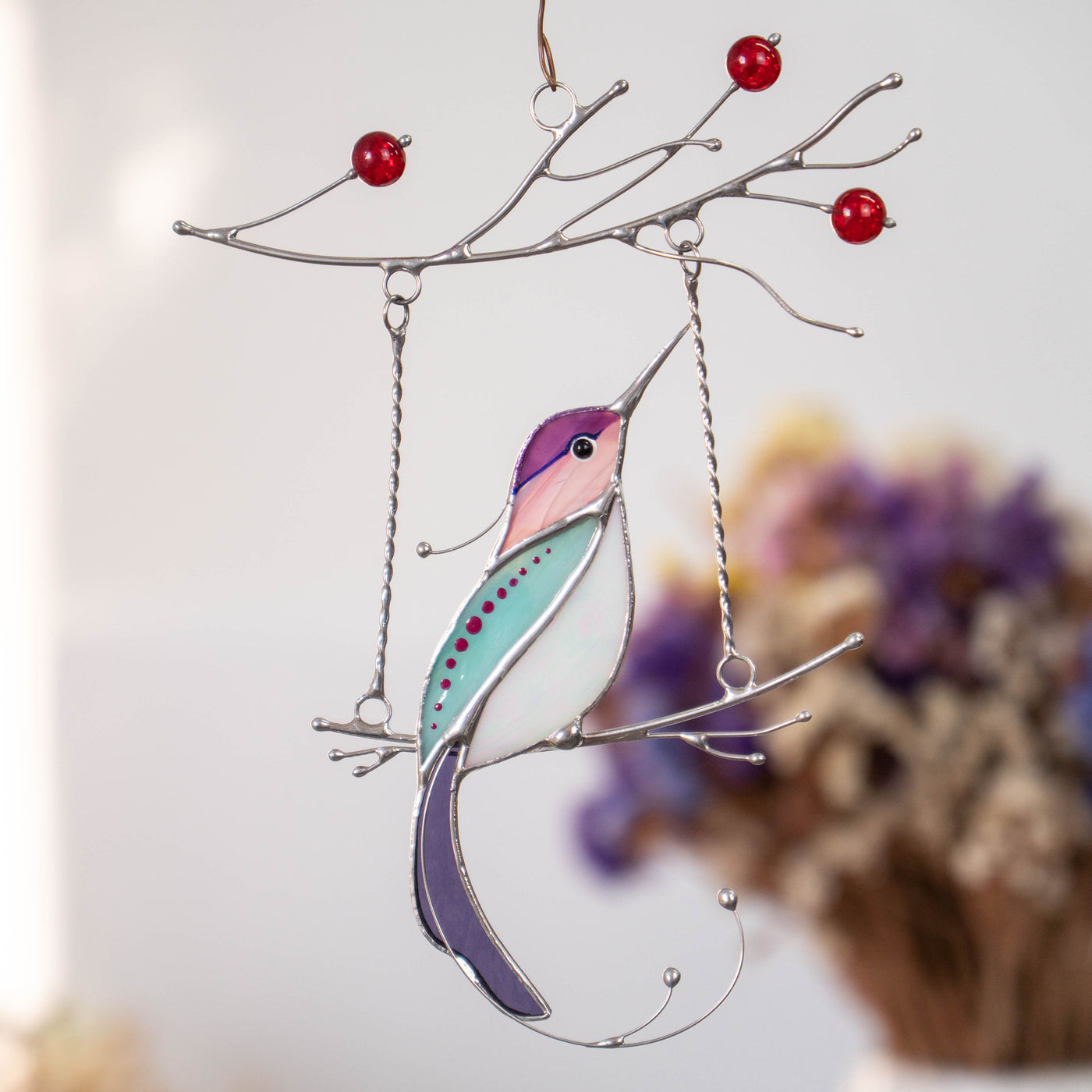 Zoomed purple hummingbird with white belly on the swing suncatcher of stained glass