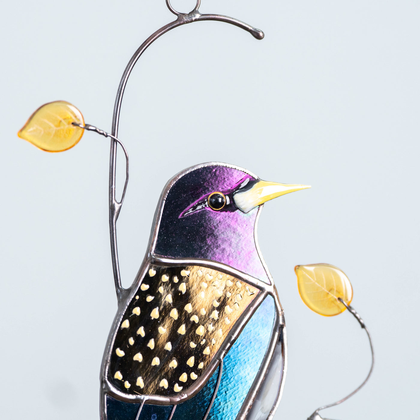 Side view of robin glass suncatcher with warm-colored leaves, hanging with white background.