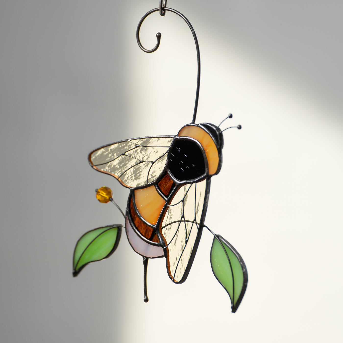 Side view of bumble bee stained glass suncatcher with sunlit background.