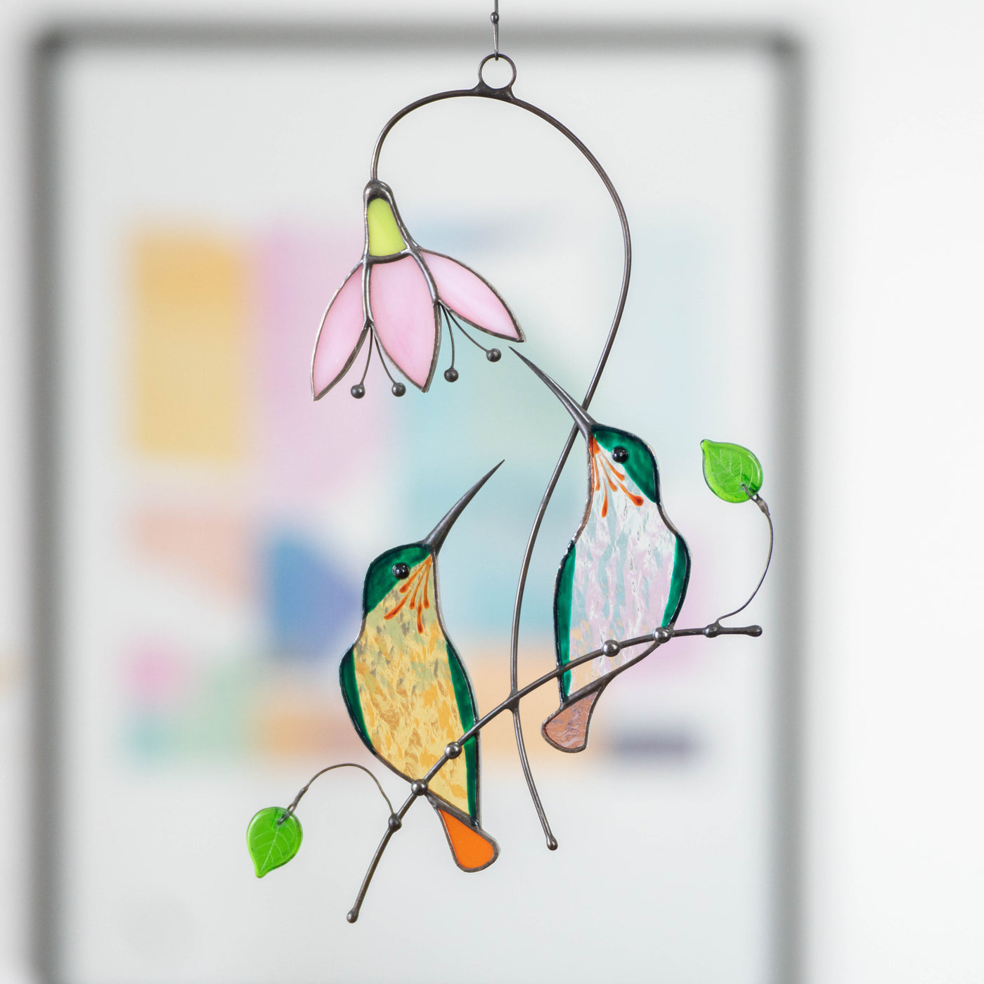 Stained glass couple of green hummingbirds sitting on the branch with pink flower.