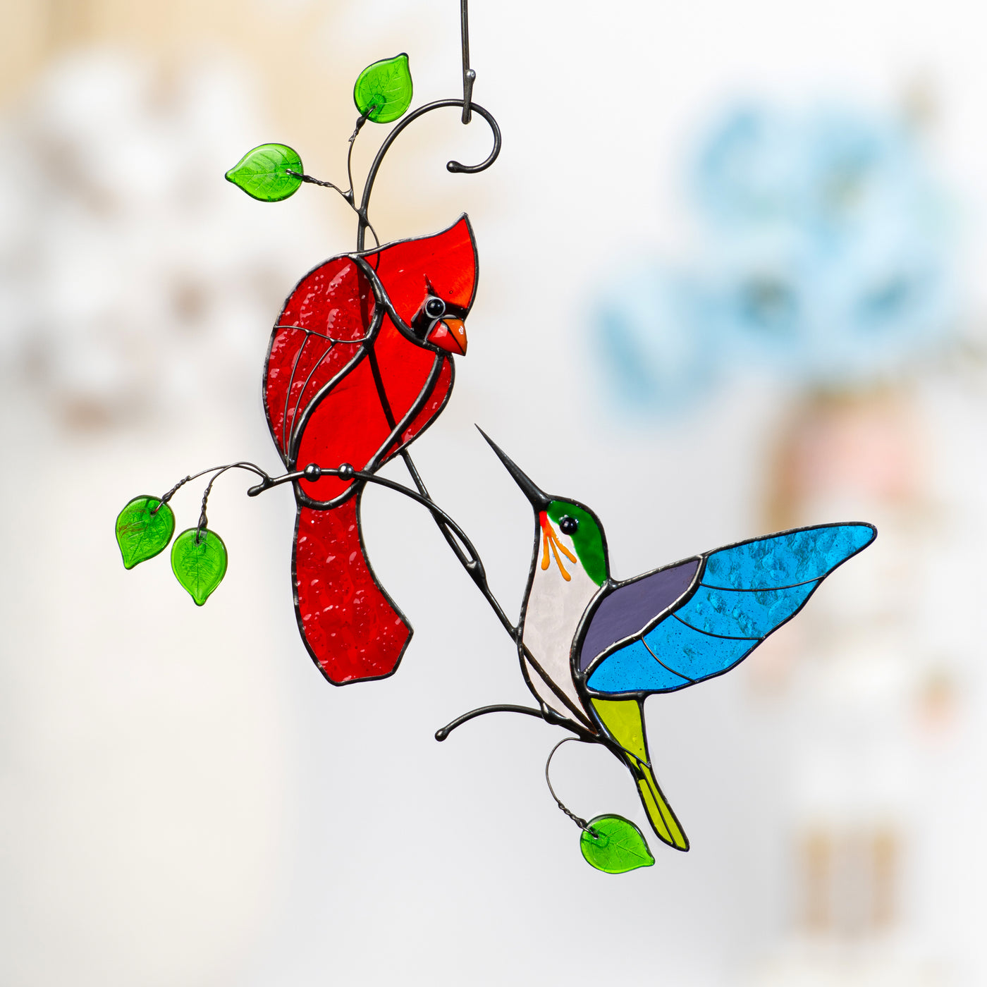 Stained glass window hanging with red cardinal and colorful hummingbird on metal branches with green glass leaves.