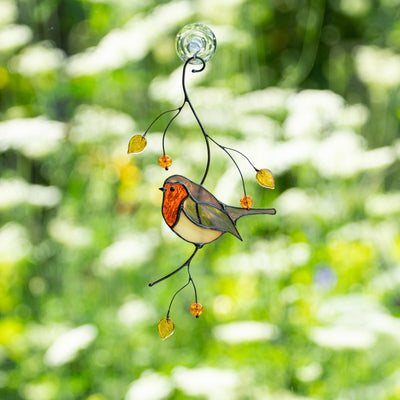 Full stained glass robin suncatcher hanging on window, decorated with yellow leaves and amber beads against a sunny garden.