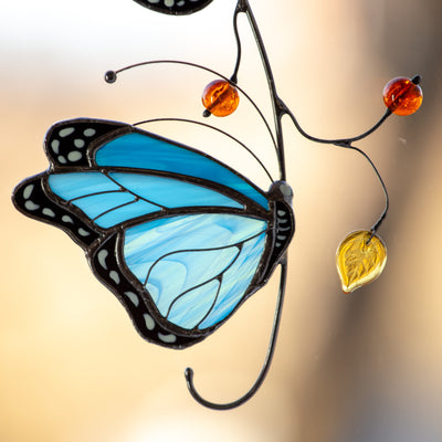 Zoomed stained glass suncatcher of a blue butterfly with leaves and berries