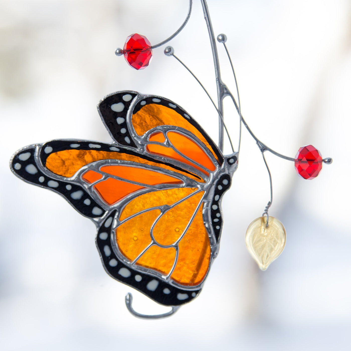 Stained glass monarch suncatcher hanging outdoors among tree branches.