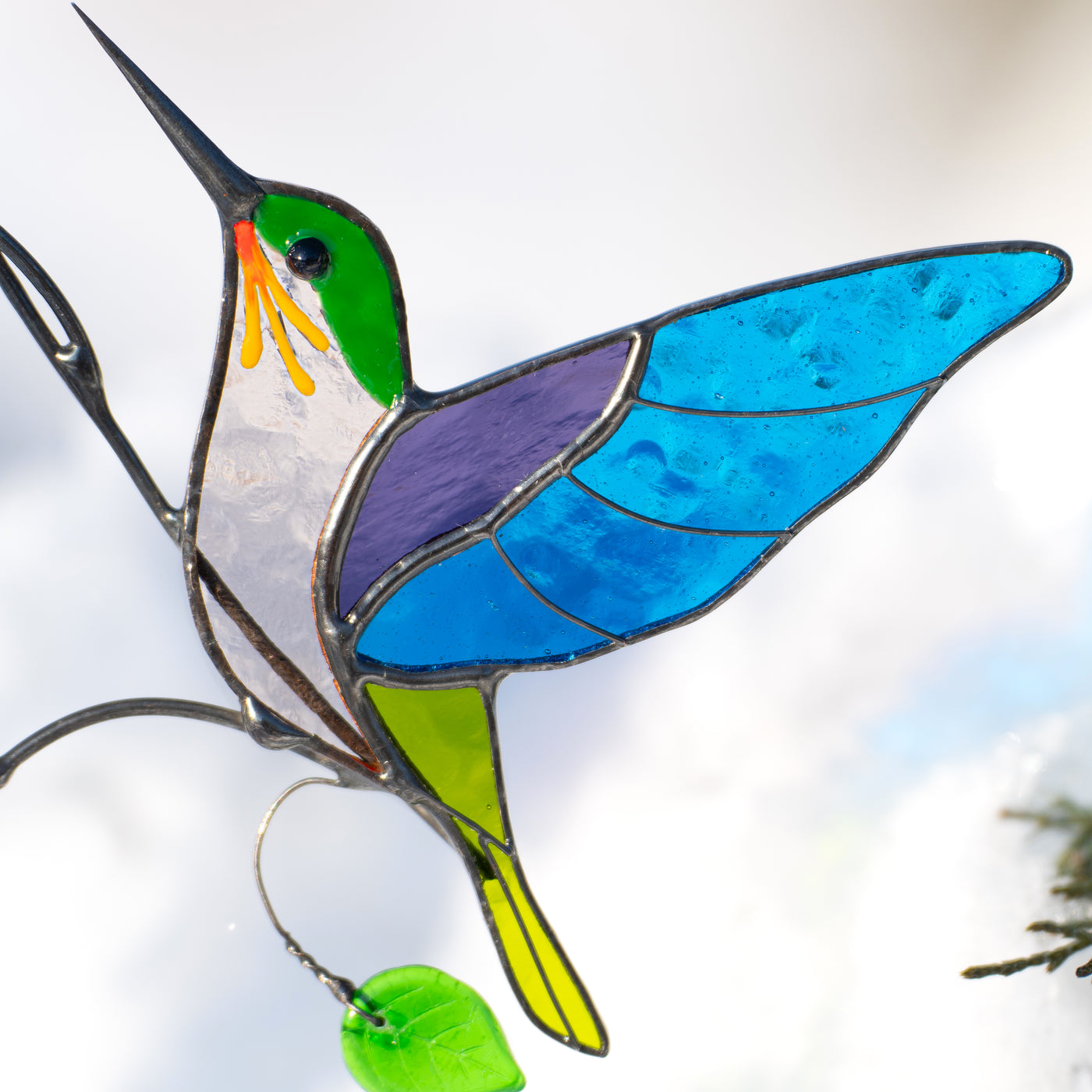 Close-up of stained glass hummingbird with blue wings, green head, and yellow tail.