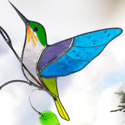 Close-up of stained glass hummingbird with blue wings, green head, and yellow tail.