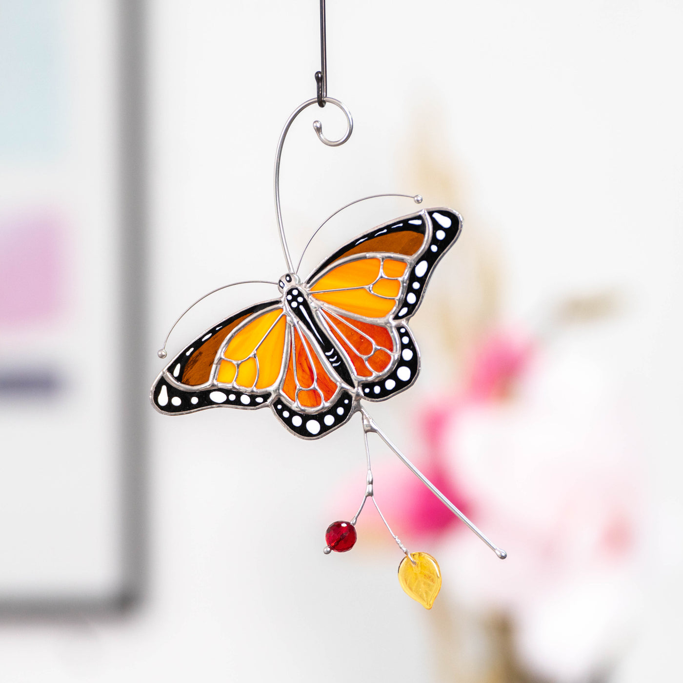 Monarch butterfly suncatcher against a blurred background with pink flowers.