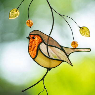 Close-up of a stained glass robin with a vibrant red chest, yellow glass leaves, and beads hanging on black wire branches.