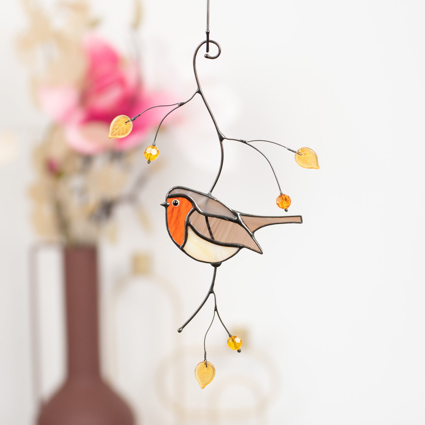 Close-up of stained glass robin hanging with yellow beads, symbolizing renewal and warmth in soft indoor light