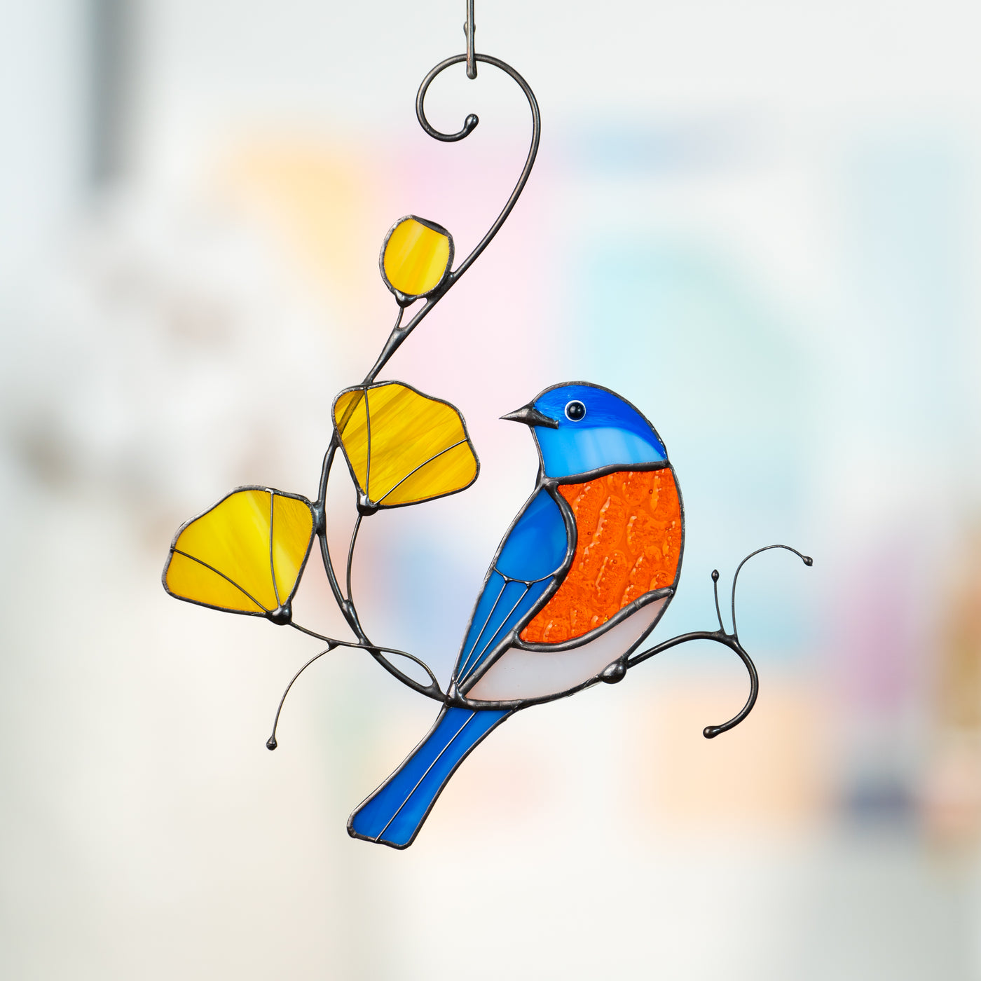 Bright stained glass bird in blue and orange sitting on a wire branch with yellow glass flowers