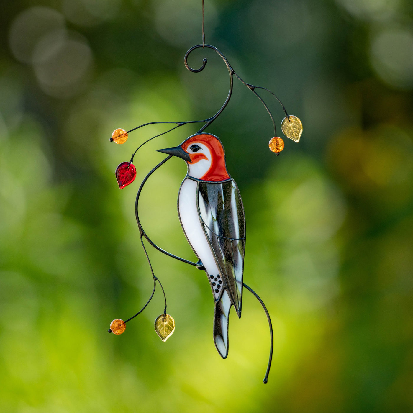 Hanging stained glass woodpecker suncatcher with red head, black and white body, and golden glass leaves on green background.