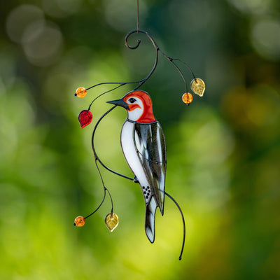 Hanging stained glass woodpecker suncatcher with red head, black and white body, and golden glass leaves on green background.