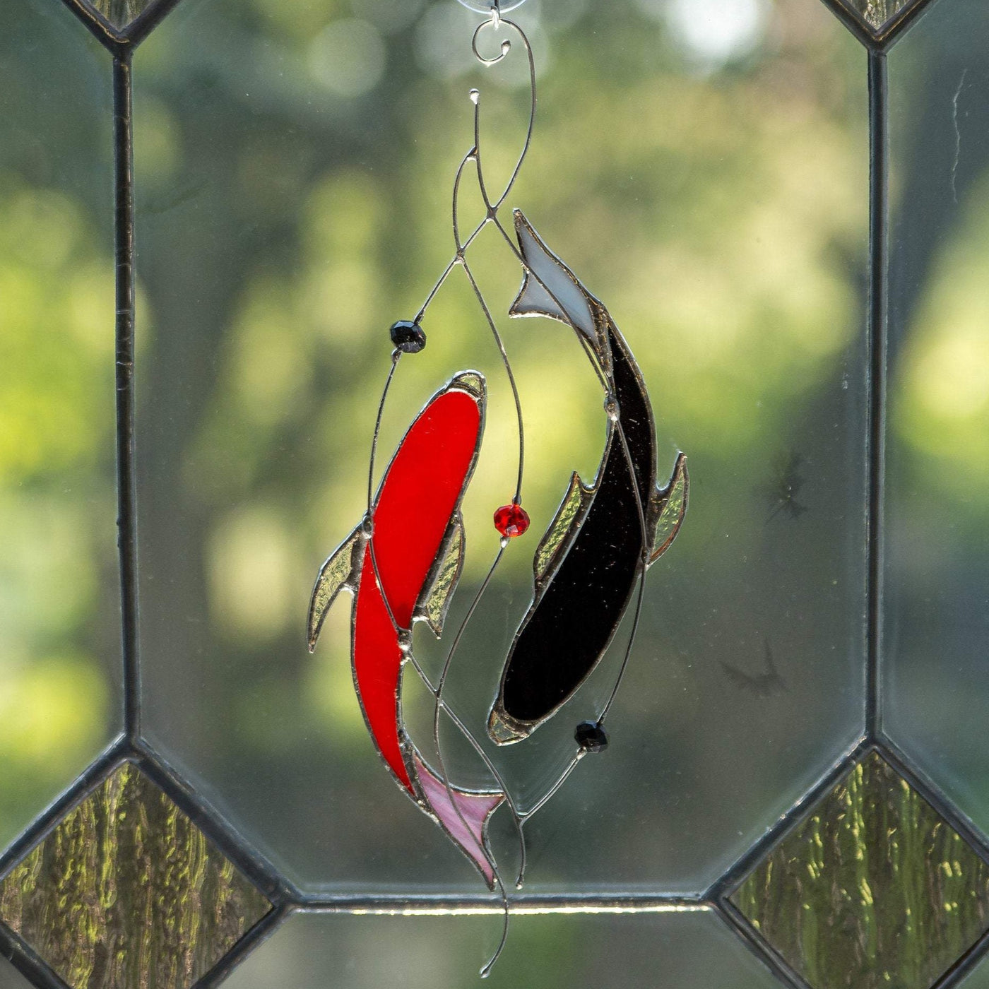Window hanging of stained glass red and black fishes representing yin yang