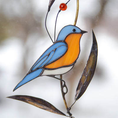 Stained glass suncatcher of a bluebird on the branch with brass leaves